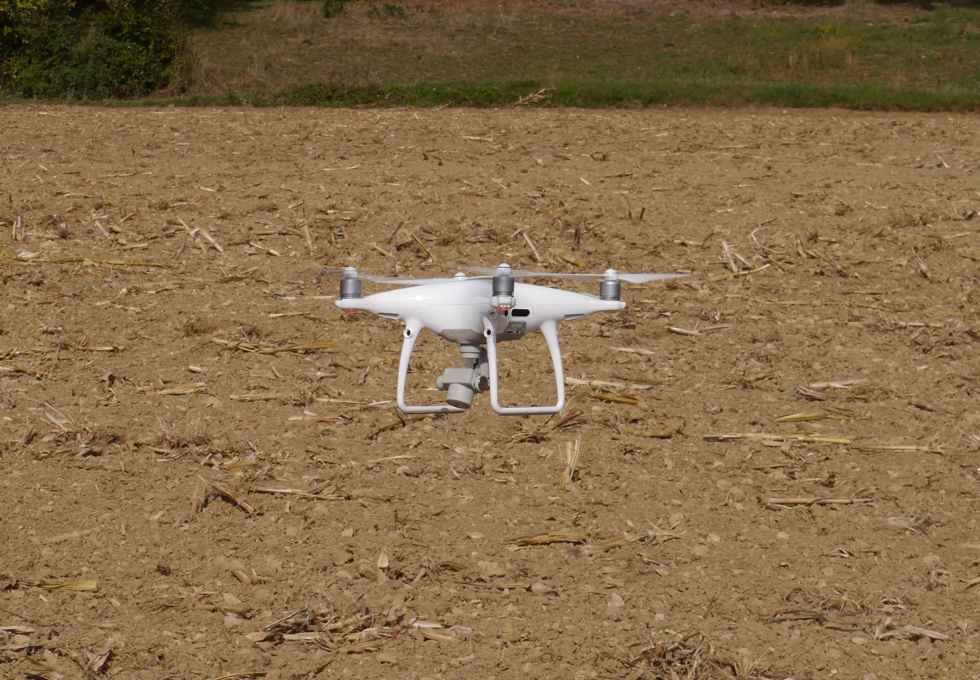 In geringer Höhe über einer abgeernteten Ackerfläche schwebt eine weiße Foto-Drohne mit vier Propellern