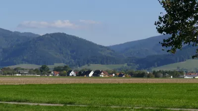 Schild mit Aufschrift "Wasserschutzgebiet". Im Hintergrund Wiesen- und Ackerflächen sowie bewaldete Hänge des Schwarzwalds.