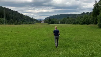 Foto zeigt einen Mann, der über eine mit Bäumen gesäumte Wiese auf ein Brunnenhaus zugeht