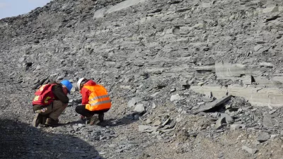 Zwei Personen knien vor den grauen Schiefern in einem Steinbruch.