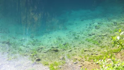 Foto zeigt die Wasseroberfläche einer Karstquelle mit Farbübergang vom flachen, gelbgrünen Uferbereich bis ins türkisblaue tiefe Wasser