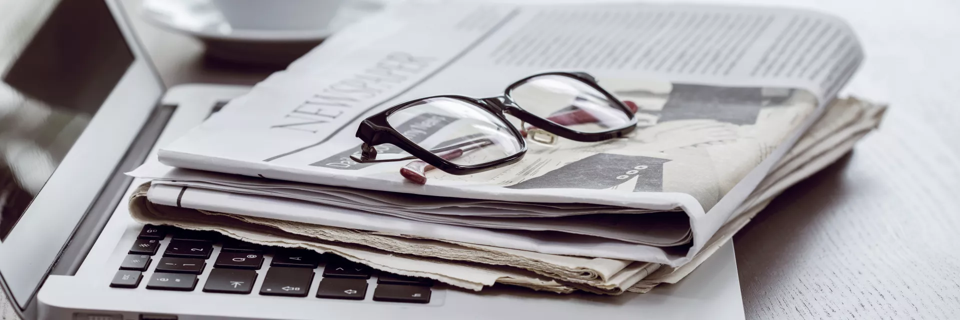 Laptop mit Zeitung und Brille; im Hintergrund eine Kaffeetasse