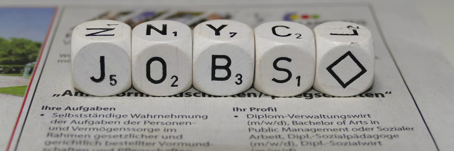 Auf einer Zeitung mit Stellenangeboten liegen Würfel, die mit den Buchstaben "J", "O", "B", und "S" beschriftet sind