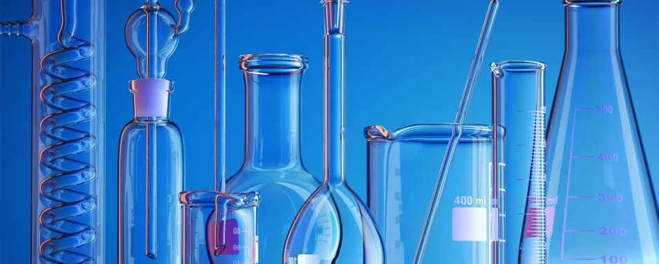Auf dem Foto sind verschiedene Glasgefäße aus einem chemischen Labor zu sehen. Die verschiedenen Bechergläser, Erlenmeyerkolben, Messzylinder, Rundkolben und Destillierzylinder stehen vor einem blauen Hintergrund.