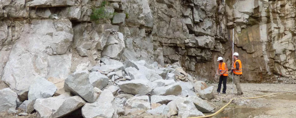 Zwei Personen stehen vor einem Geröllhaufen in einem Steinbruch.